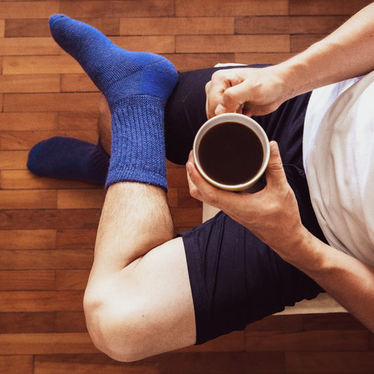 Person sitting wearing blue socks and holding a cup of coffee.
