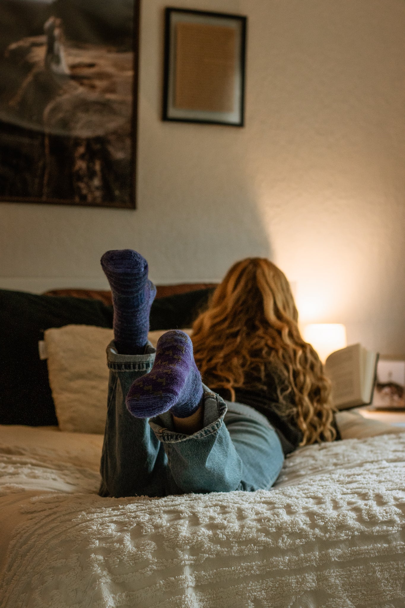 Person with feet up on a bed in a cozy room with warm lighting.