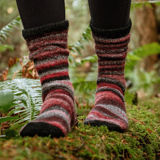 Striped socks worn on a person's feet standing on a mossy forest floor.